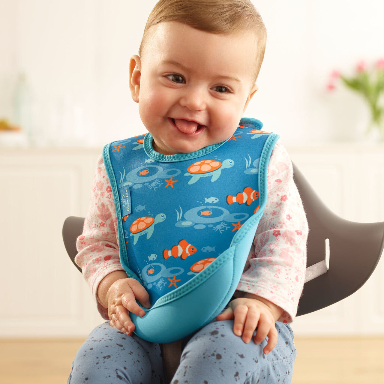 Baby wearing a blue bib with ocean-themed design, sitting on a chair.