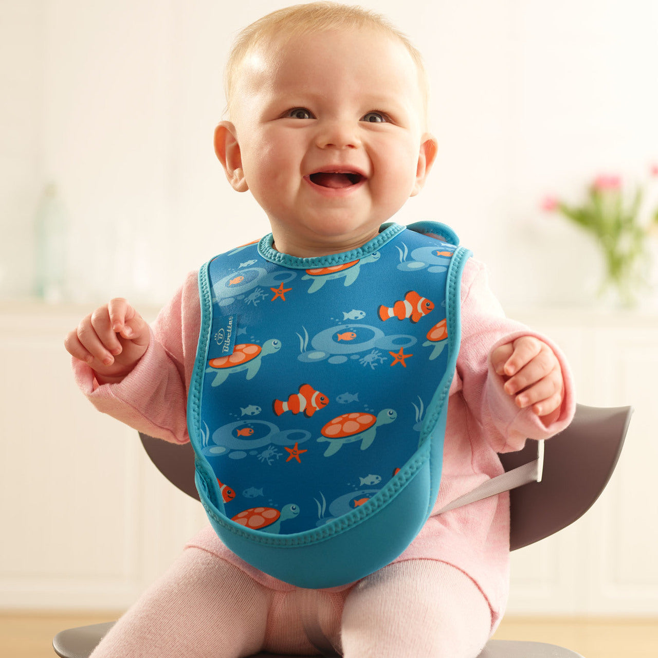 Baby wearing a blue bib with fish pattern, sitting on a chair.