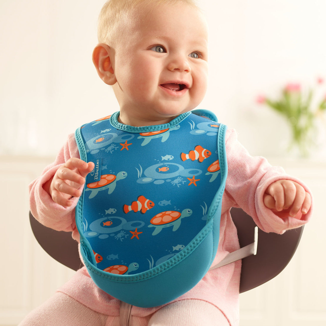 Baby wearing a blue bib with ocean-themed design, sitting in a high chair.