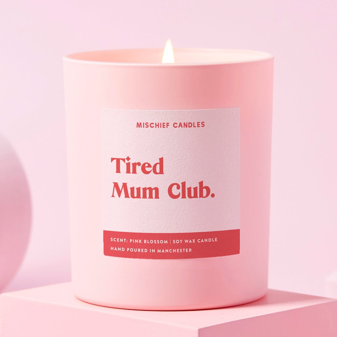 Pink candle labeled 'Tired Mum Club' by Mischief Candles on a pink background