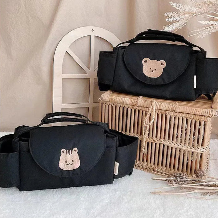 Black diaper bags with bear embroidery on a textured surface with a wicker basket in the background.