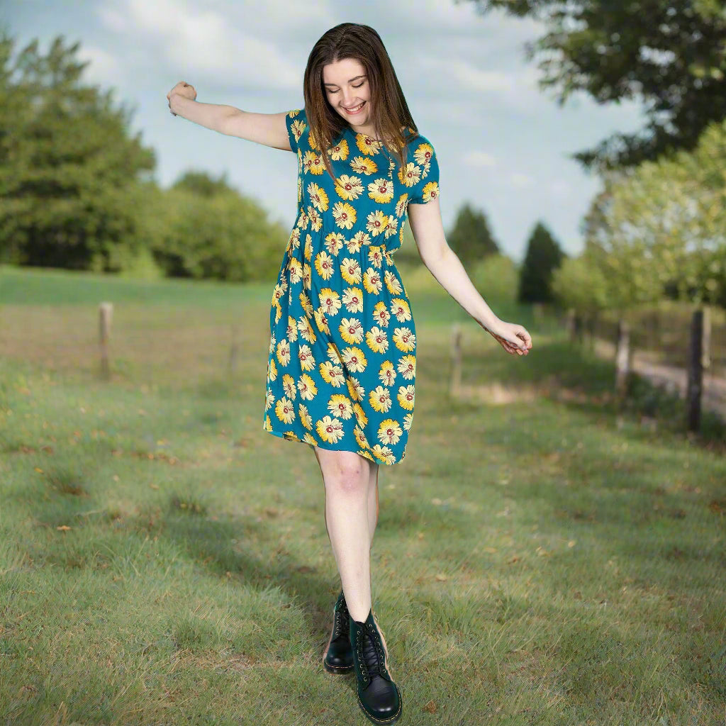 Woman in a floral dress standing in a grassy field with trees in the background