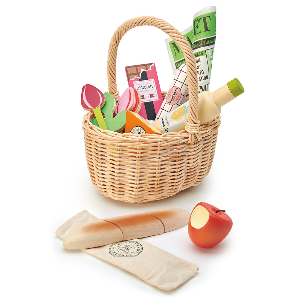 Wicker basket with toys, including a newspaper, banana, and apple, on a white background.