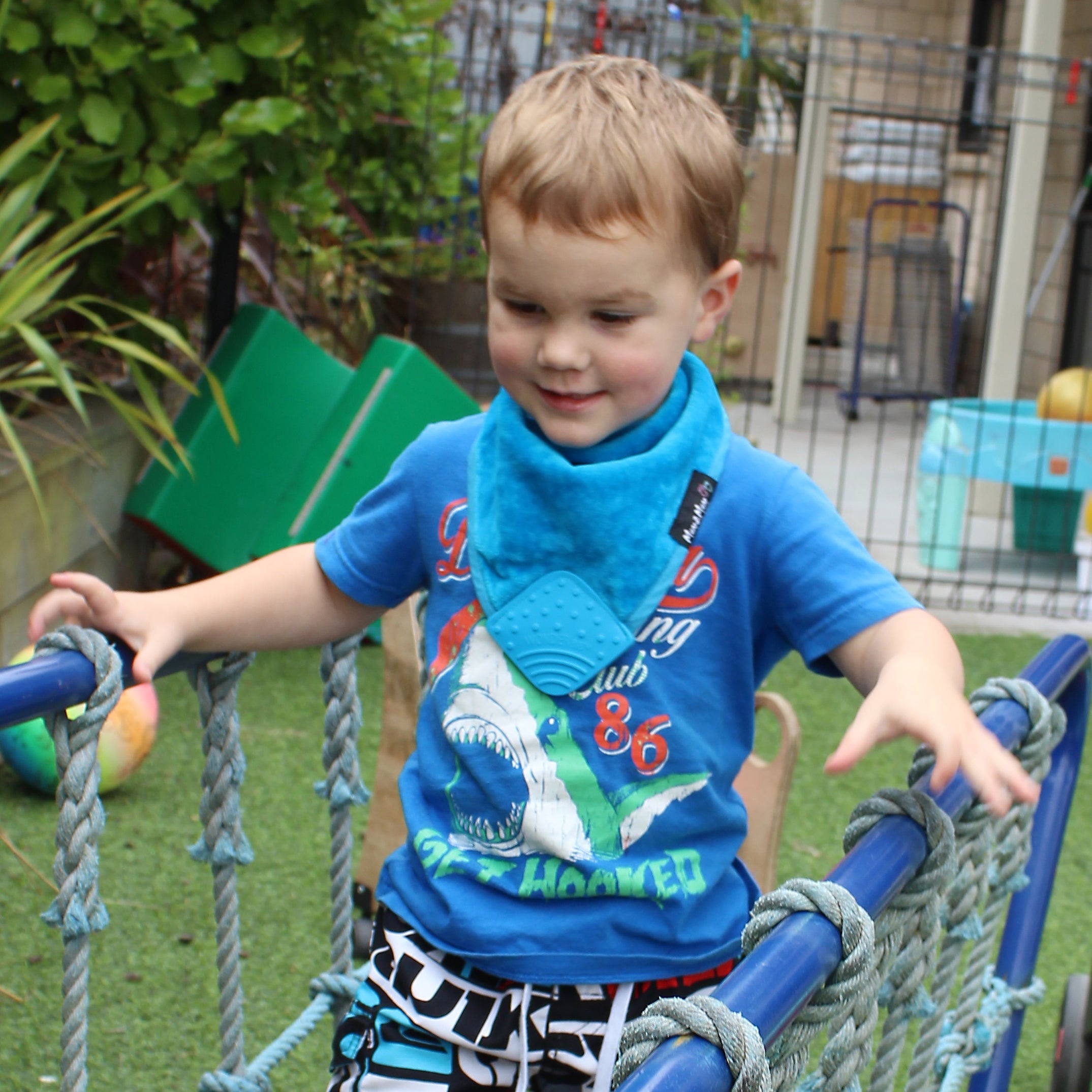 Child playing on a playground structure with a blue shirt and black shorts.