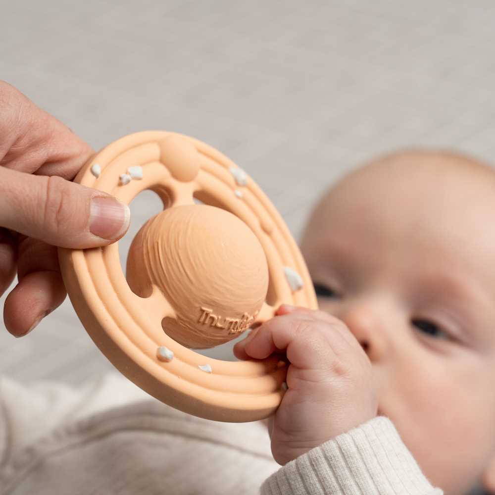 Baby holding a peach-colored teething ring with a blurred background