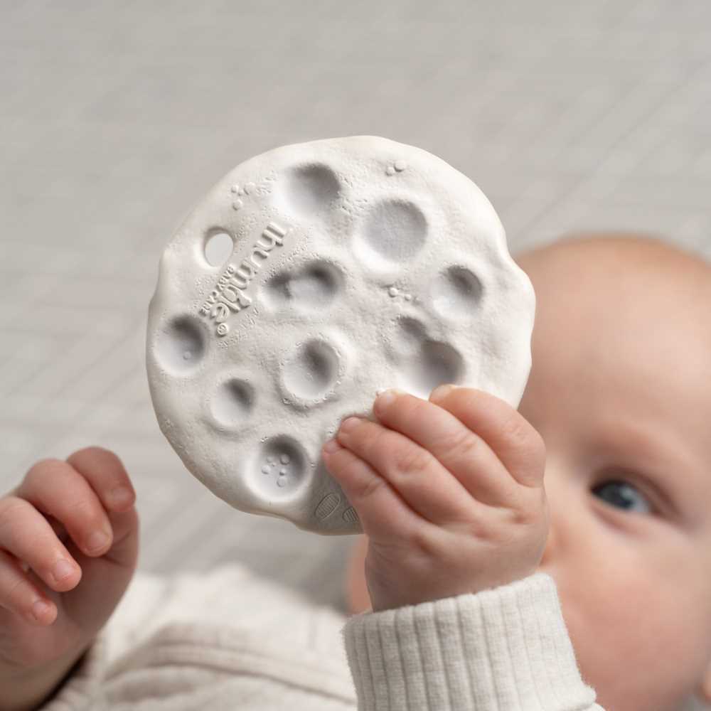 Baby holding a textured round object against a neutral background
