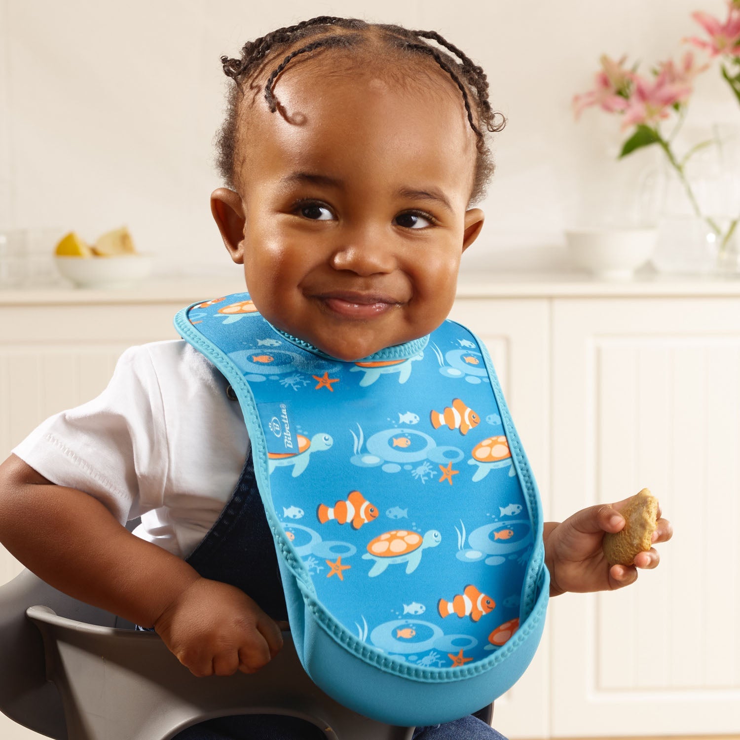 Child wearing a blue bib with sea-themed design, sitting in a high chair.