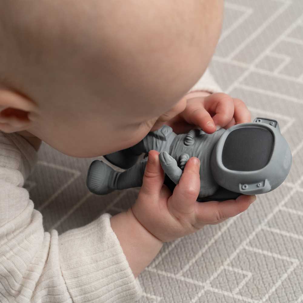 Baby holding a gray toy resembling a robot on a patterned surface