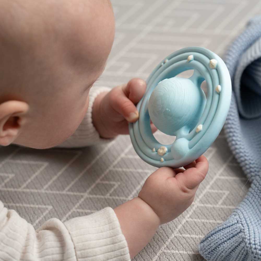 Baby holding a blue teething ring on a patterned surface