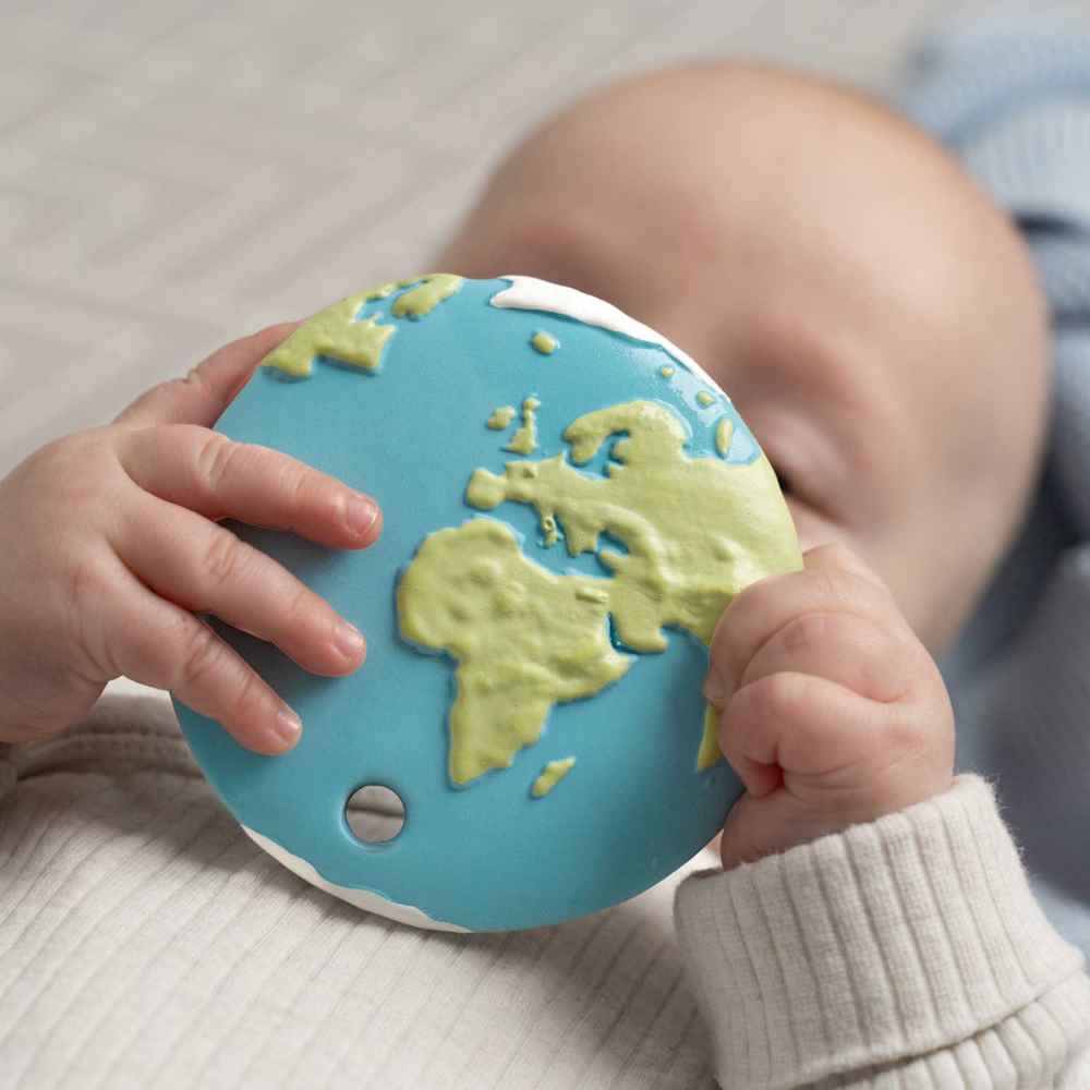 Child holding a blue and green world map teething toy