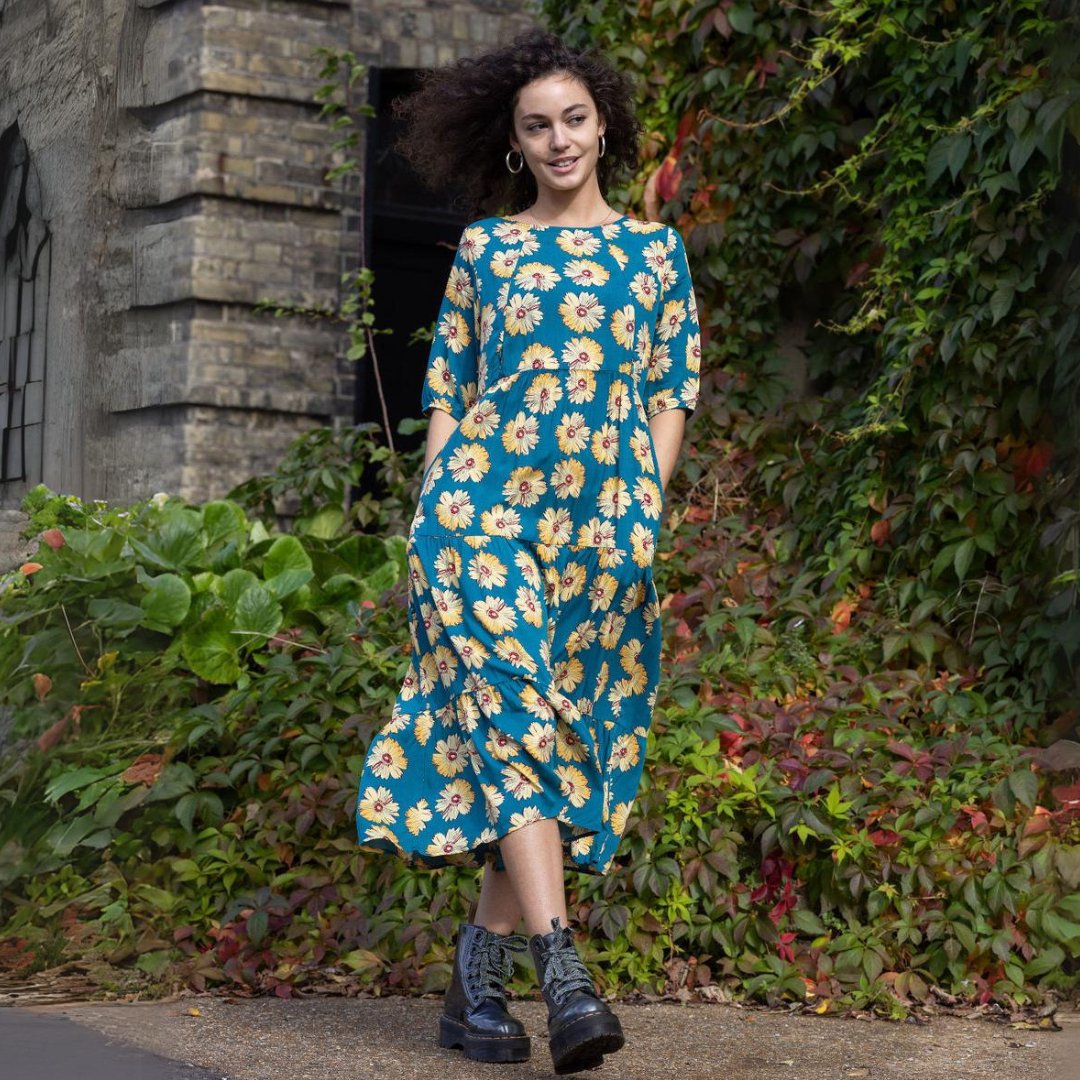 Woman wearing a blue floral dress standing in front of a stone wall and greenery