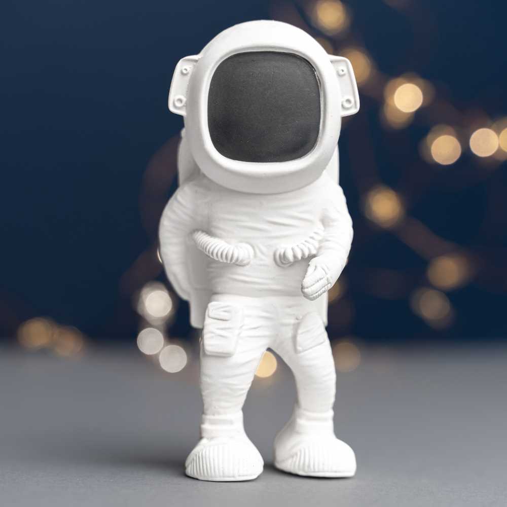 White ceramic astronaut figurine on a dark background with blurred lights